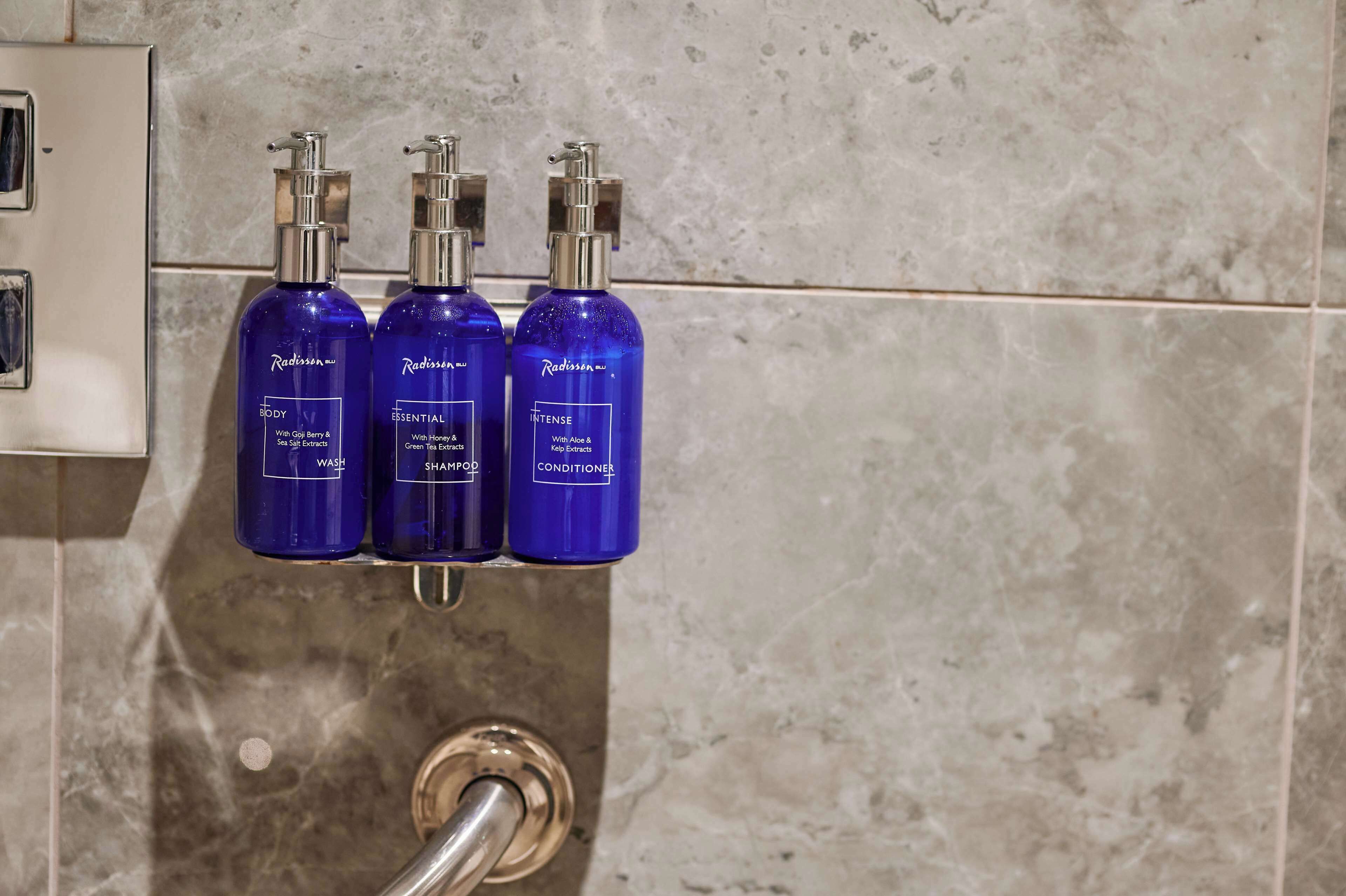 Three blue bottles of Radisson body wash, shampoo, and conditioner on a wall-mounted shelf.