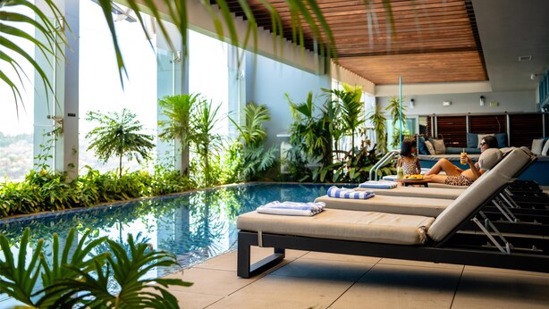 Un área de piscina interior moderna con sillones de descanso y plantas tropicales.