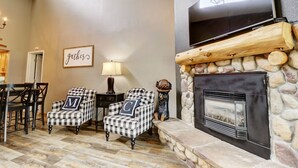 A cozy living room with a stone fireplace, checkered armchairs, a television, and a 'gather' sign on the wall. - Large, Welcoming Condo With Incredible Views - WL406 by Redawning (Copper Mountain)