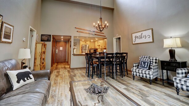 A spacious living room with a leather couch, a glass coffee table, and a dining area with a chandelier. - Large, Welcoming Condo With Incredible Views - WL406 by Redawning (Copper Mountain)