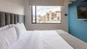 Una habitación de hotel moderna con una cama grande, vistas a la ciudad a través de una ventana y una pared de acento azul.