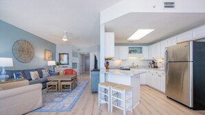 Eine moderne Küche mit weißen Schränken, einem Edelstahl-Kühlschrank und einem Essbereich mit Sofa und Tisch.