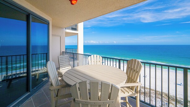 Ein Balkon mit Tisch und Stühlen mit Blick auf Strand und Meer.