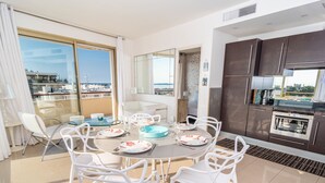 Un'area pranzo moderna con un tavolo rotondo, sedie bianche e vista sul mare attraverso ampie finestre.