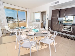 Un comedor moderno con una mesa redonda, sillas blancas y vistas al mar a través de amplios ventanales.
