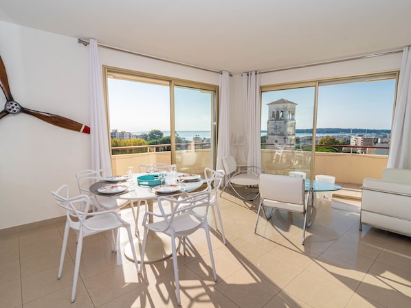 A modern apartment with a balcony, large windows, and a dining area set up for four people.