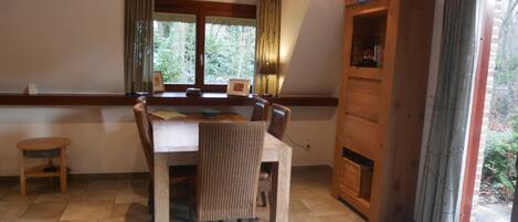 Een eetruimte met een houten tafel en stoelen, een klein krukje, en een houten kast met een open haard.