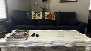 A living room with a dark blue sofa, a white coffee table with a floral pattern, and a carpet with a circular design. - SKI, FISH, GOLF, RAFT, HIKE, HUNT, ATV ride, RELAX, 4 bdr home on wooded ADK lot (Malone)