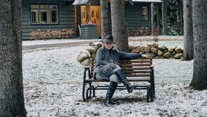 A person sitting on a bench in a snowy outdoor area with trees and a building in the background. - SKI, FISH, GOLF, RAFT, HIKE, HUNT, ATV ride, RELAX, 4 bdr home on wooded ADK lot (Malone)