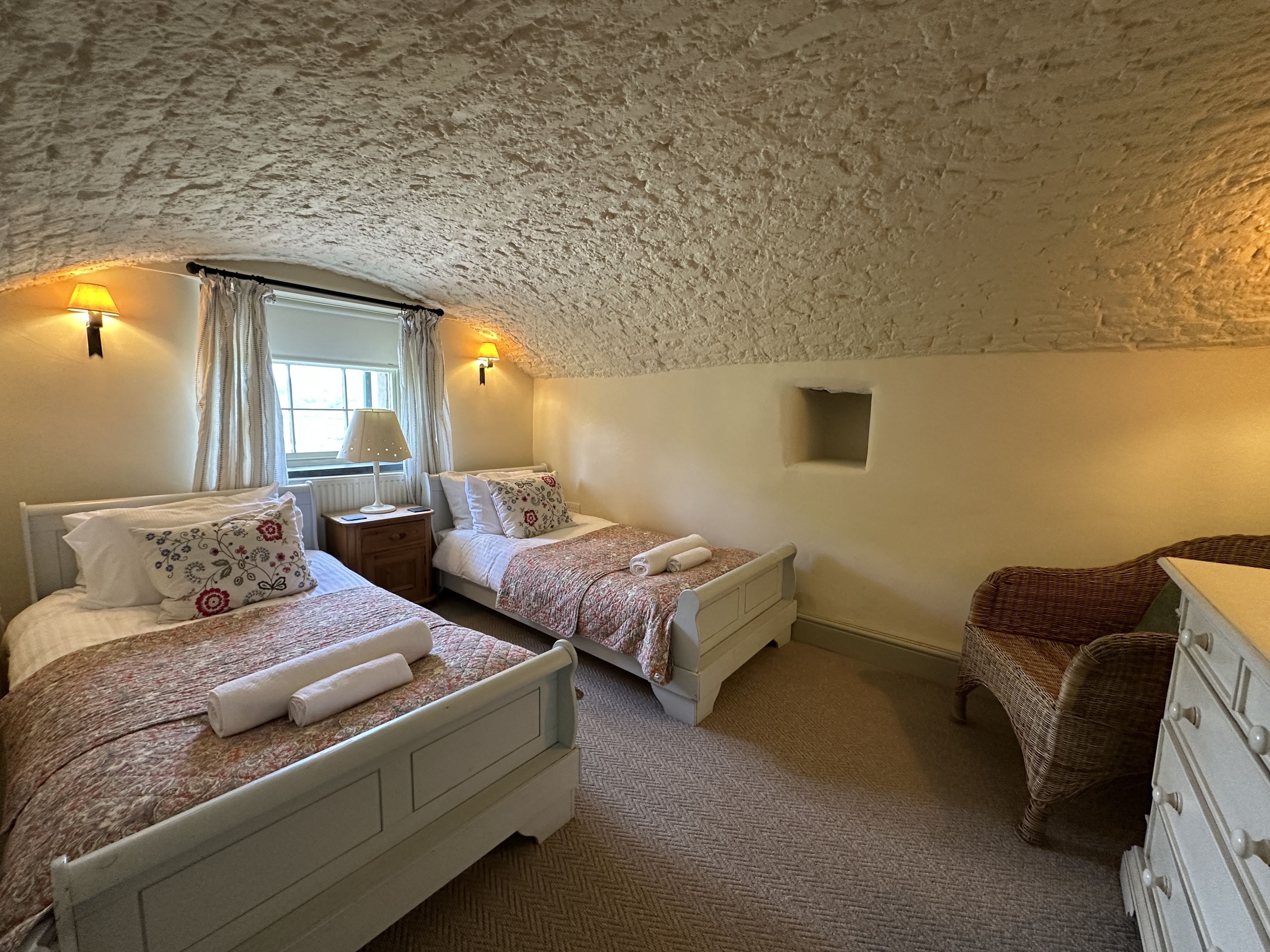 Une chambre avec deux lits, une commode, une chaise et une fenêtre avec des rideaux.