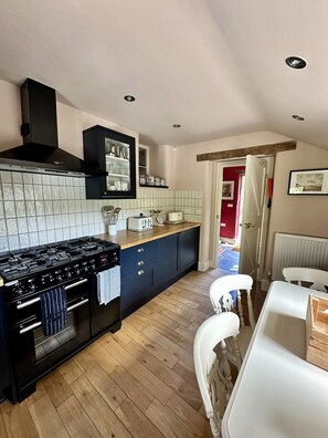A modern kitchen with a black stove, white tiles, and wooden flooring.