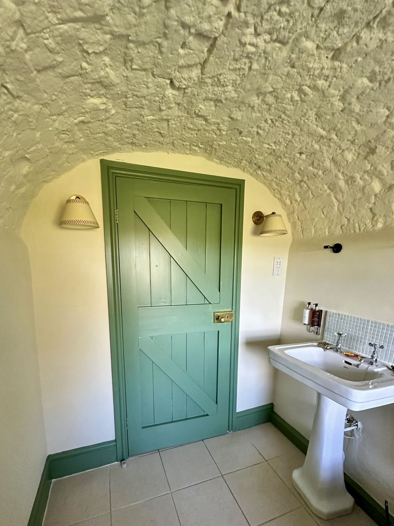 Un baño con puerta verde, lavamanos blanco y techo con textura.