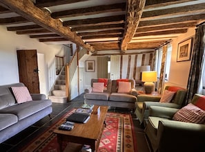 A rustic interior with exposed wooden beams, a staircase, a sofa, a coffee table, and a lamp.