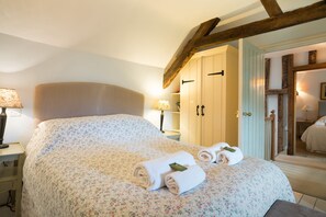 Un lit bien fait, avec une literie à motifs floraux et des serviettes enroulées, une poutre en bois au plafond et une armoire en bois avec une porte.