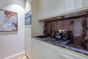 A modern kitchen with white cabinetry, a marble backsplash, and a coffee machine.