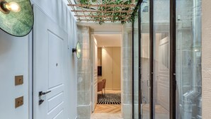 A hallway with a white door, a glass door, and a wooden pergola with plants.