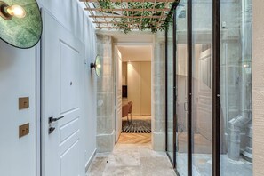 A hallway with a white door, a glass door, and a wooden pergola with plants.