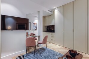 Une cuisine moderne avec des meubles blancs, un coin repas avec deux chaises roses et un téléviseur fixé au mur.