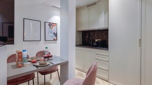 A modern kitchen with white cabinets, a marble countertop, and a dining area with pink chairs and a table set for two. - St Georges - Incredible One Bedroom with a patio (Paris)
