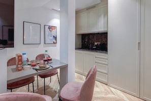 A modern kitchen with white cabinets, a marble countertop, and a dining area with pink chairs and a table set for two. - St Georges - Incredible One Bedroom with a patio (Paris)
