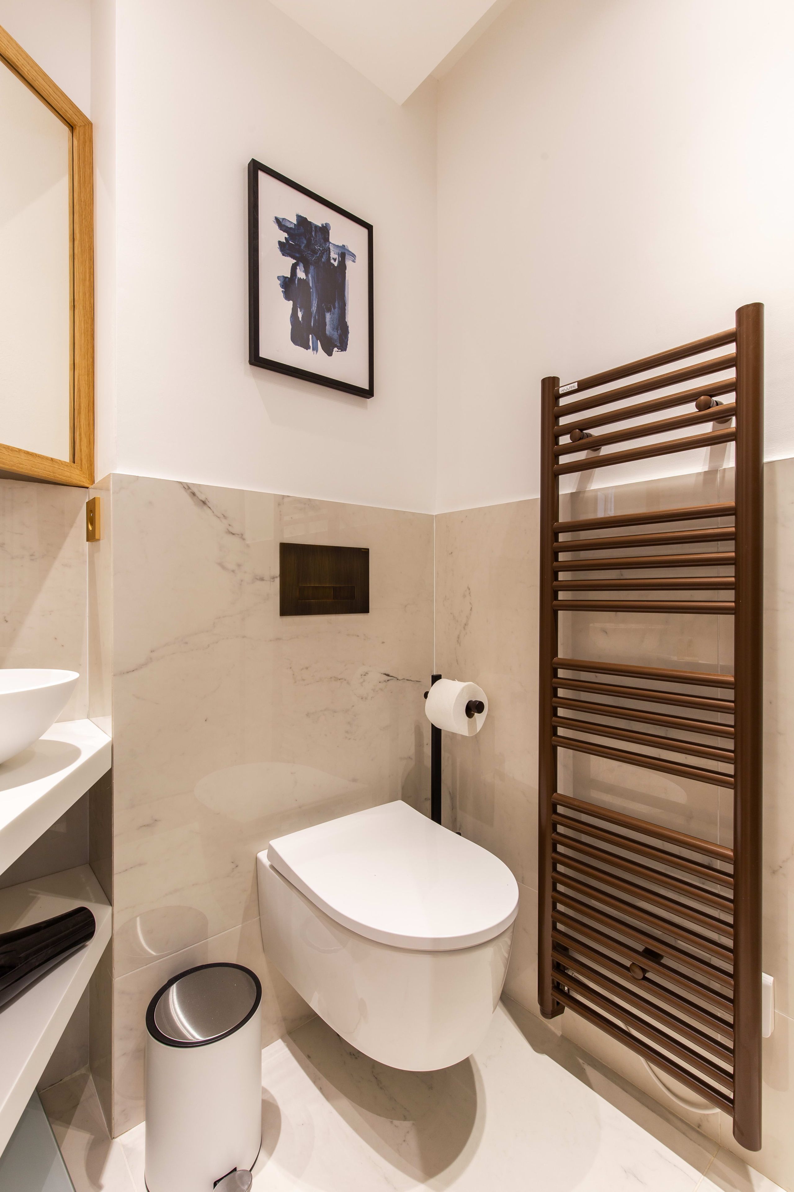 A modern bathroom with a toilet, a sink, a marble-tiled wall, a framed artwork, and a towel rack.