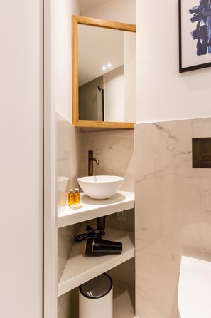 A bathroom with a white sink, a mirror with a wooden frame, and a marble wall. - St Georges - Superb studio in the heart of Paris (Paris)