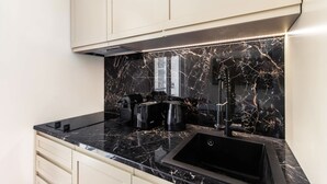 A kitchen with a black marble backsplash, a stainless steel range hood, and a black sink. - St Georges - Superb studio in the heart of Paris (Paris)