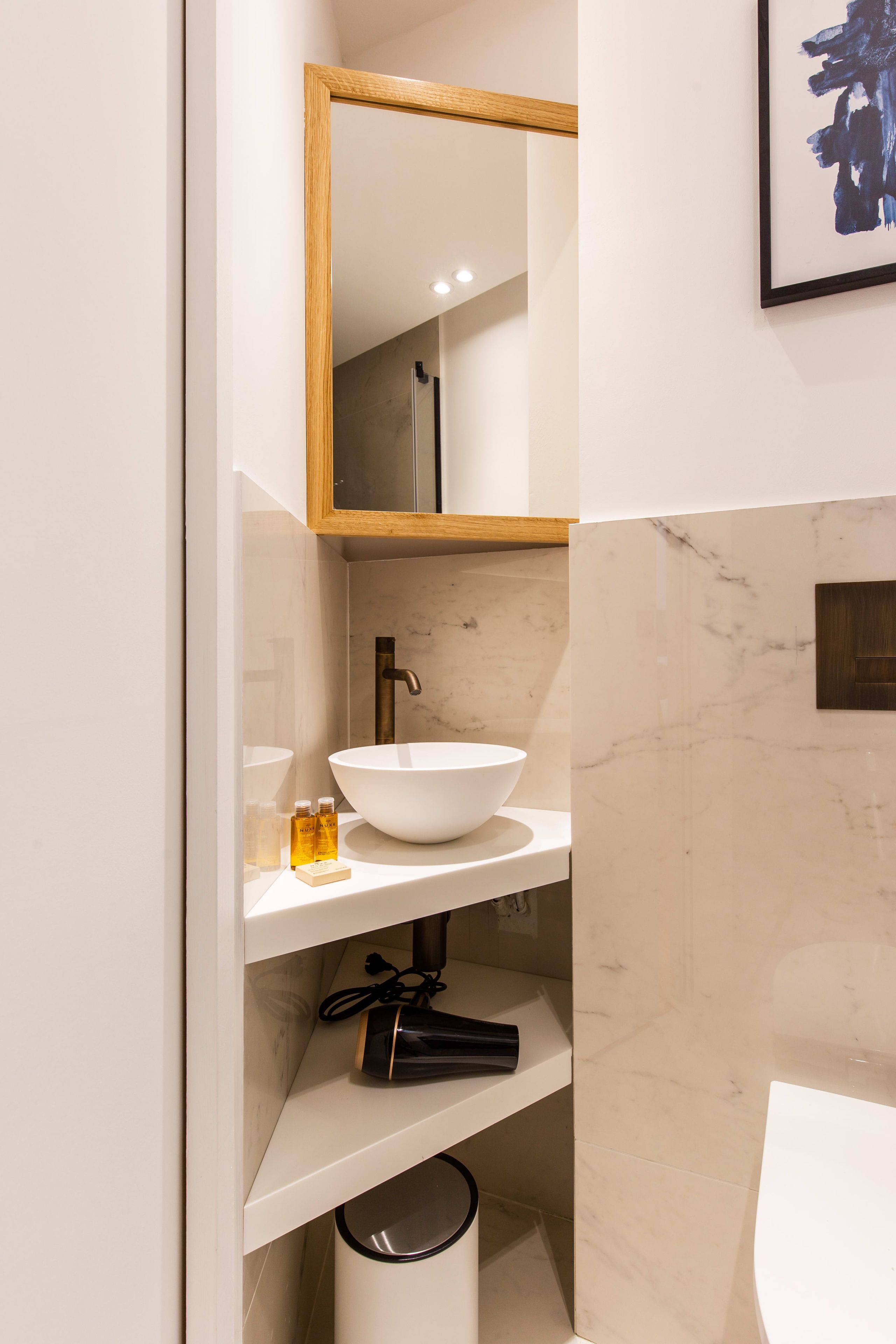 A bathroom with a white sink, a mirror, and a framed artwork on the wall.
