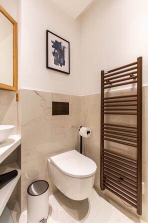 A modern bathroom with a toilet, a sink, a marble-tiled wall, a framed artwork, and a towel rack. - St Georges - Superb studio in the heart of Paris (Paris)