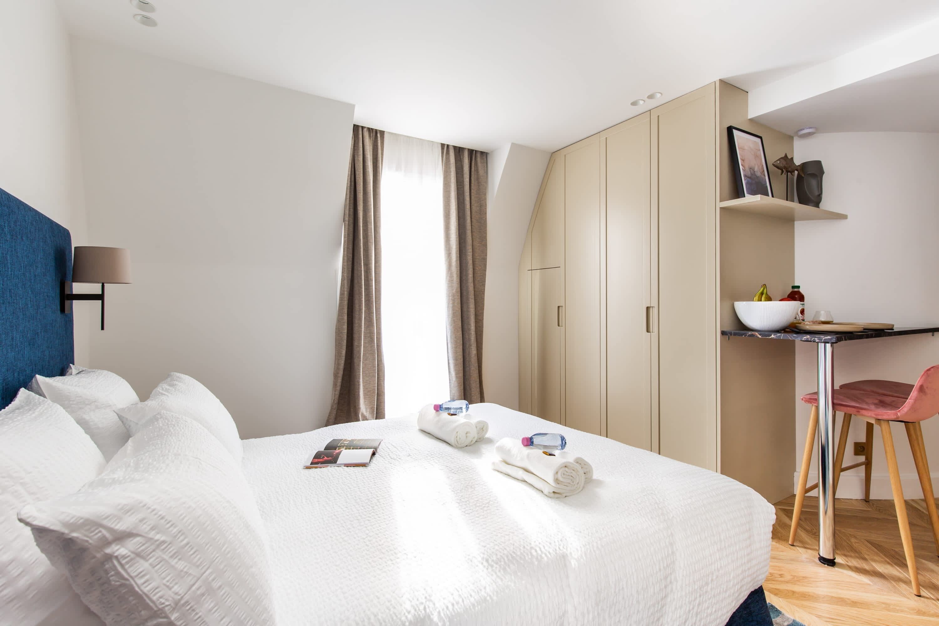 A hotel room with a bed, a desk, a chair, and a wardrobe.