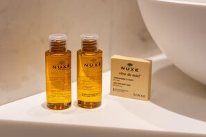 Two bottles of Nuxe shampoo and a box on a white surface.