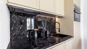 A modern kitchen with a black marble countertop, a built-in stove, and a stainless steel sink. - St Georges - One Bedroom in Paris South Pigalle (Paris)