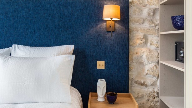 A bedroom with a stone wall, a blue headboard, a wooden bedside table with a lamp, and a white bed. - St Georges - One Bedroom in Paris South Pigalle (Paris)