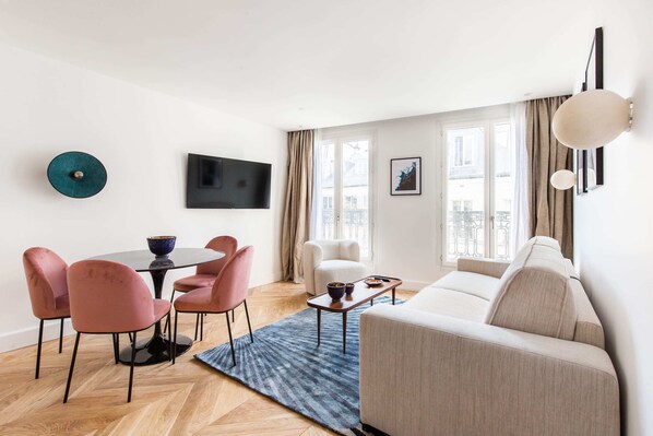 Ein modernes Wohnzimmer mit Sofa, Esstisch, Stühlen, Fernseher und Blick ins Freie.