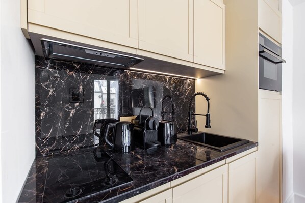 Una cocina moderna con encimera de mármol negro, estufa integrada y pileta de acero inoxidable.