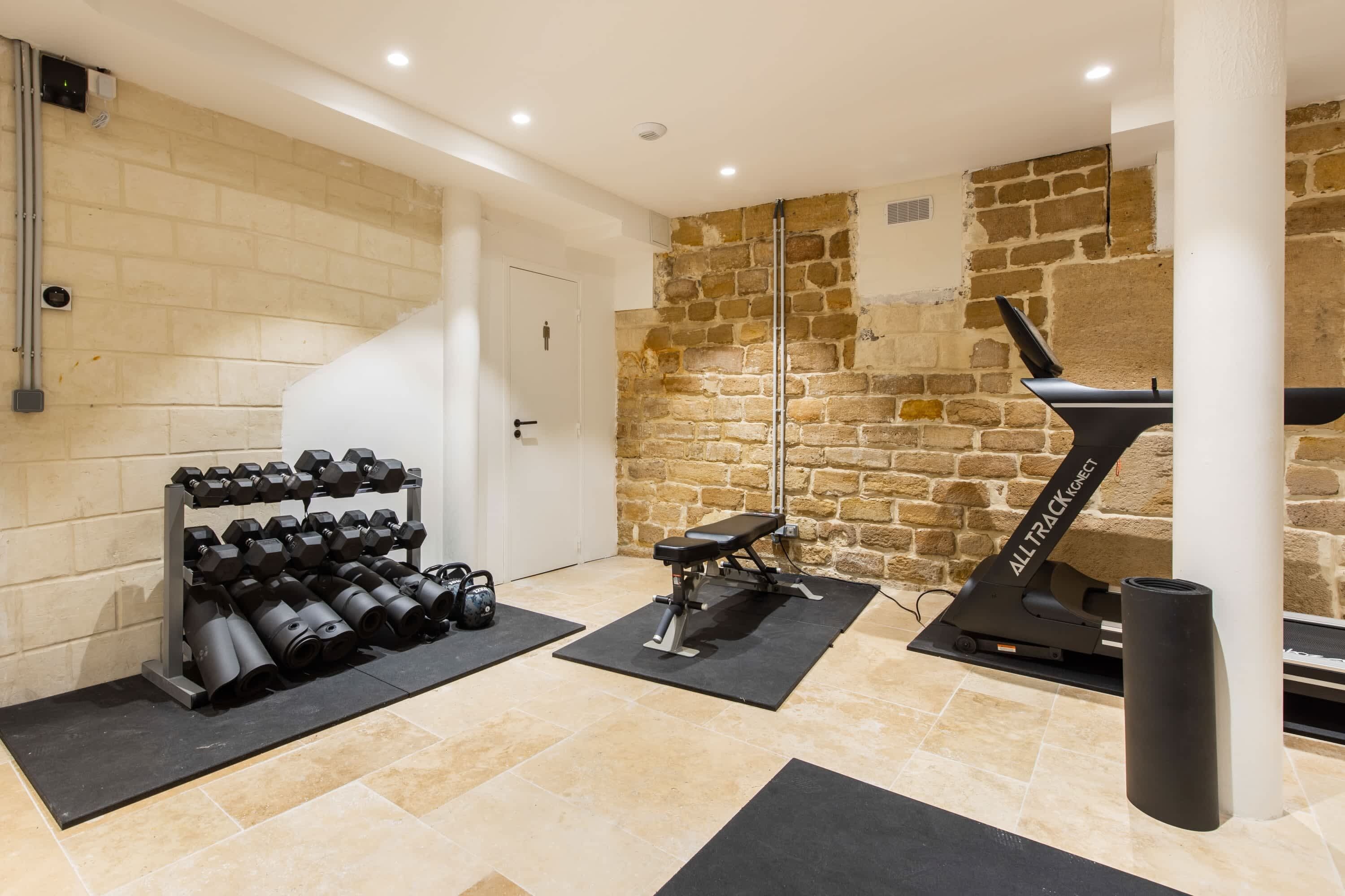 A gym with exercise equipment, a stone wall, and a door.