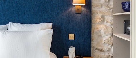 Une chambre avec un mur en pierre, une tête de lit bleue, une table de chevet en bois avec une lampe, et un lit blanc.