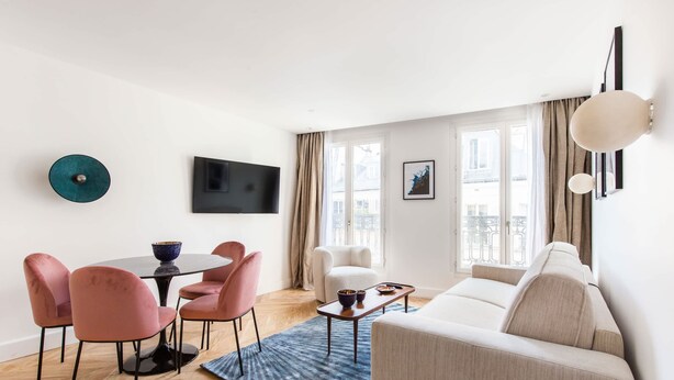 A modern living room with a sofa, a dining table with chairs, a flat-screen TV, and a large window with curtains. - St Georges - One Bedroom in Paris South Pigalle (Paris)