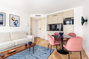 A modern living room with a sofa, a coffee table, and a dining area with pink chairs and a round table. - St Georges - One Bedroom in Paris South Pigalle (Paris)