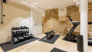 A gym with exercise equipment, a stone wall, and a door.