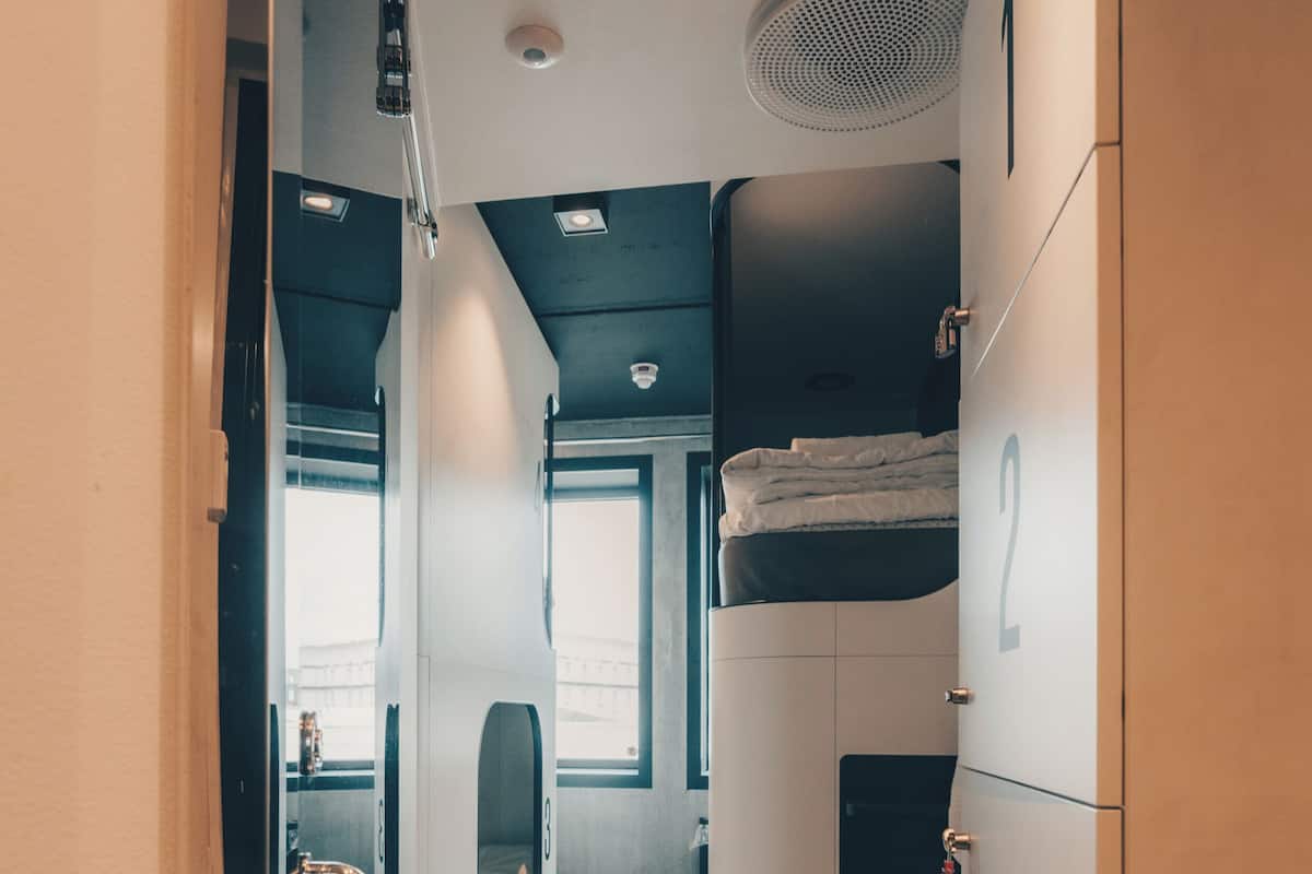 A narrow corridor with a bunk bed, a small window, and a door with a handle.