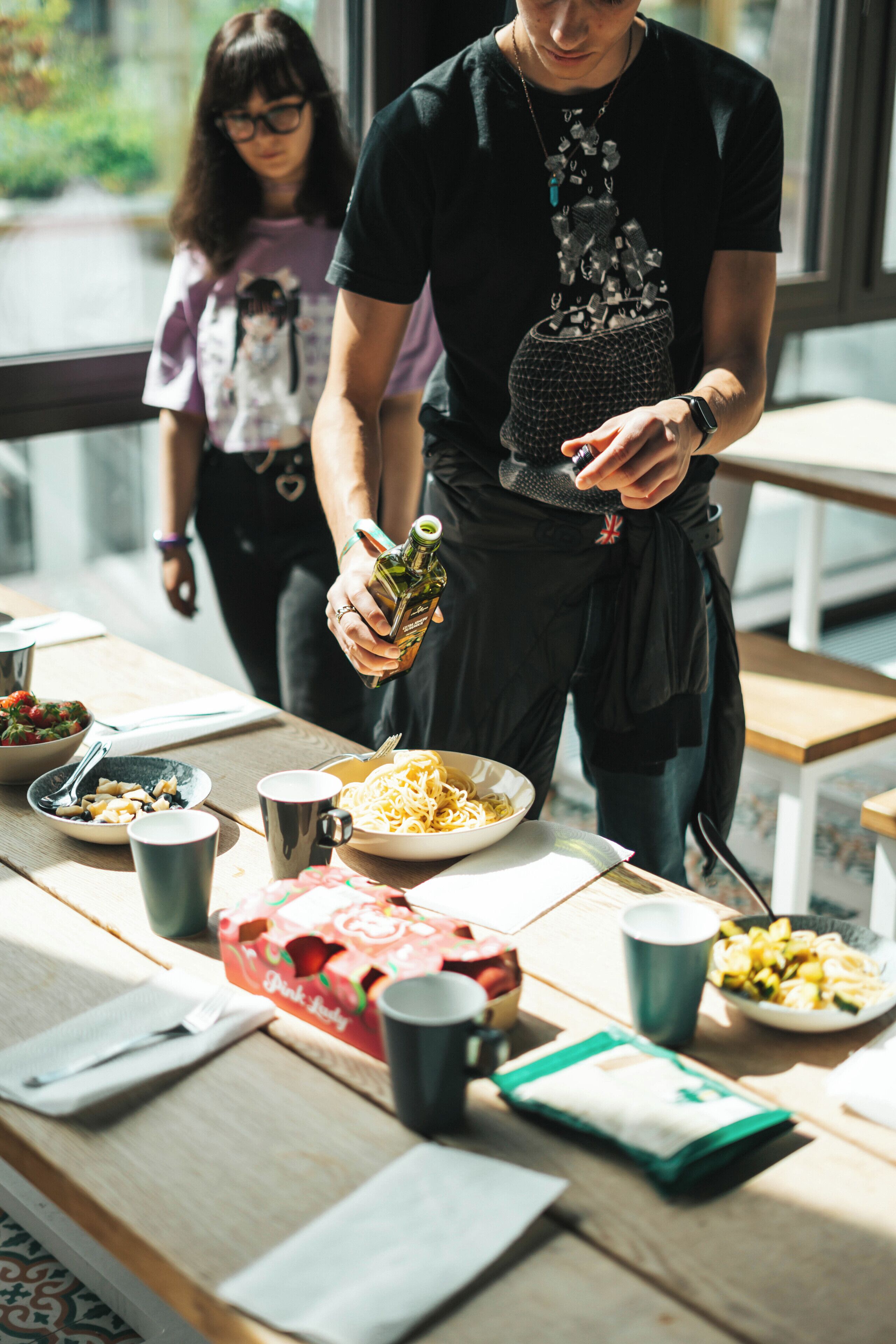 A person pouring a drink into a glass at a table with food and drinks.