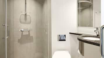 Un baño moderno con ducha de vidrio, inodoro blanco y lavamanos con encimera de granito.