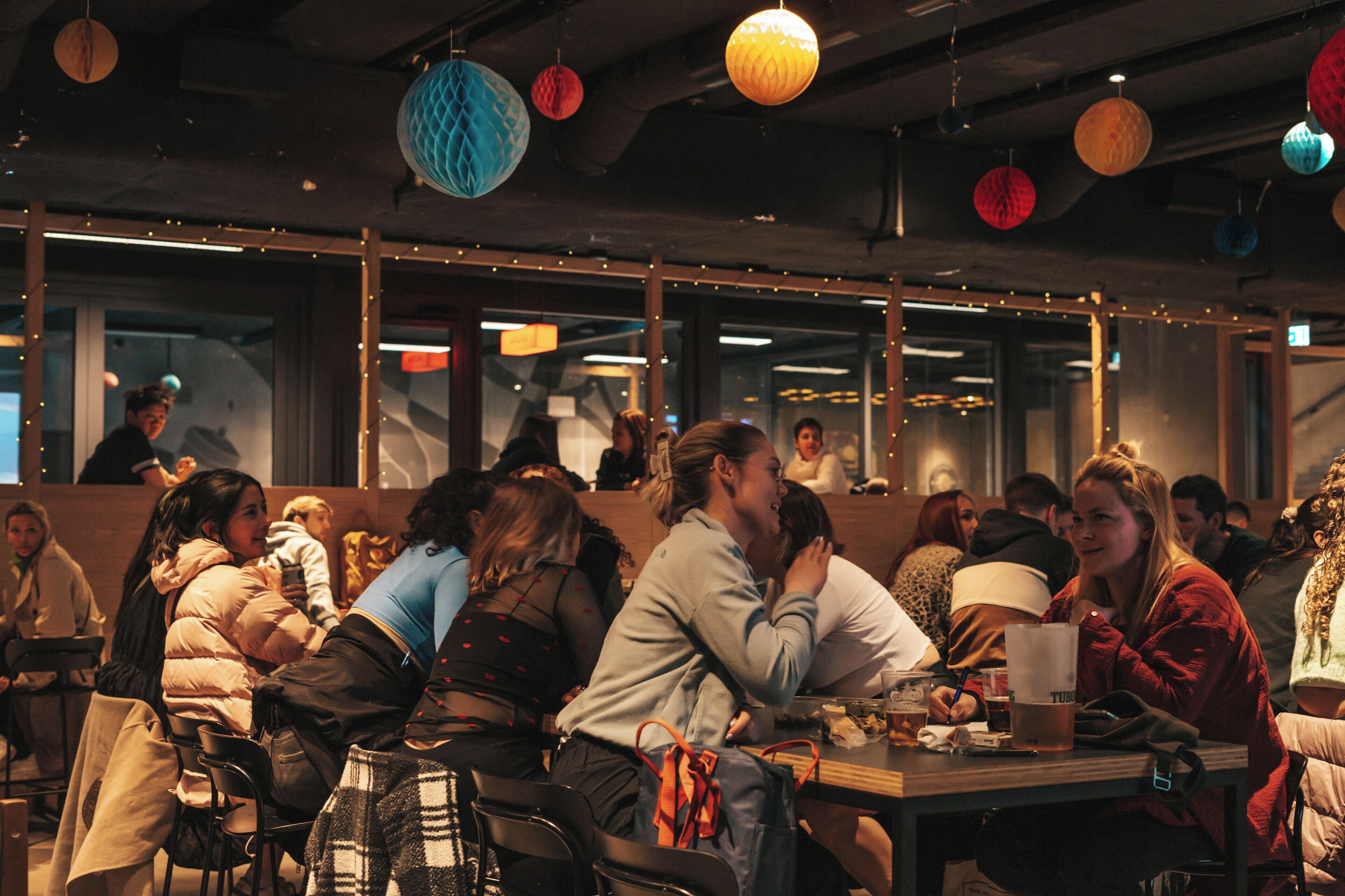 A restaurant with booths and tables, string lights, and hanging paper lanterns.
