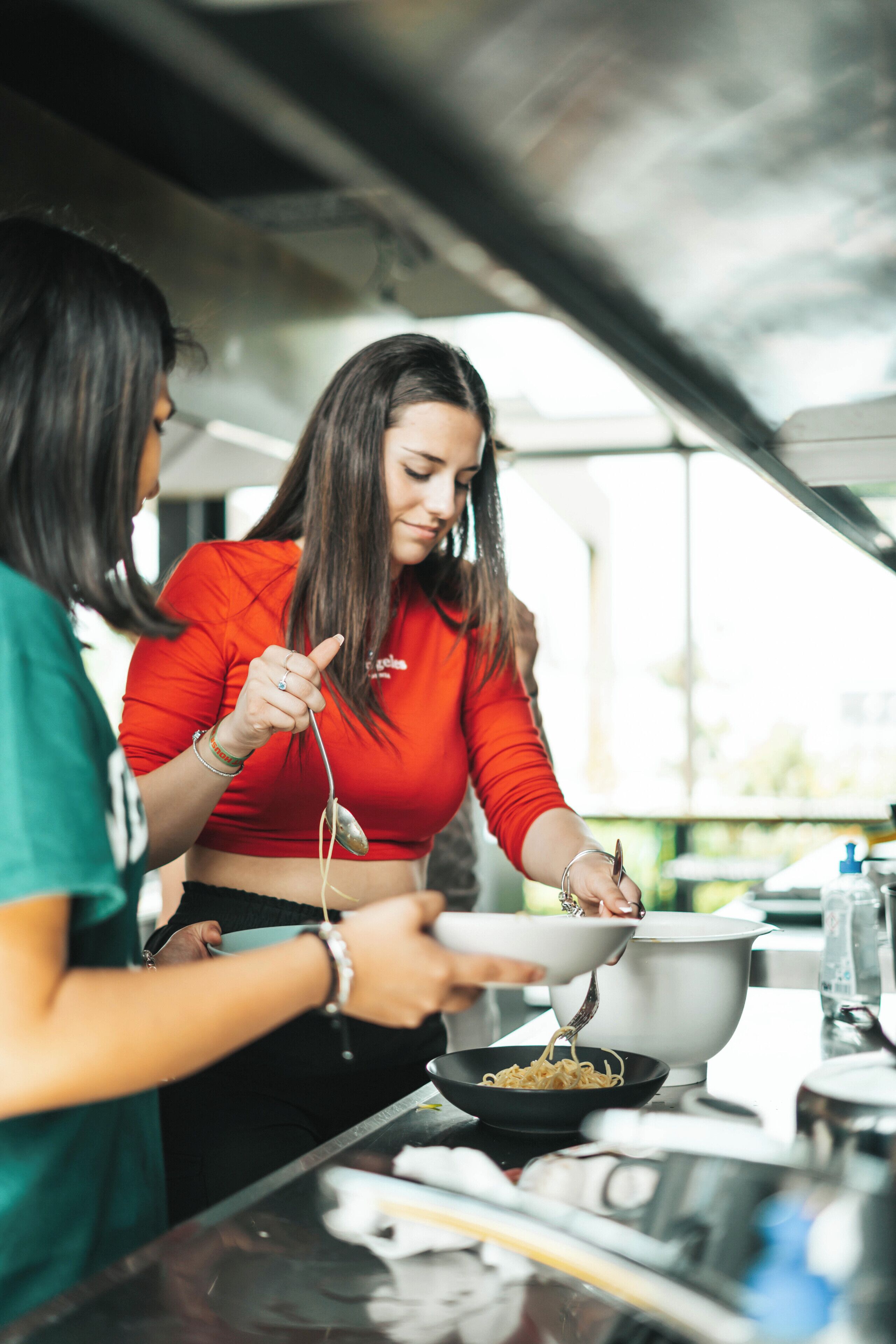Una persona cocinando fideos en una cocina con una ventana al fondo.