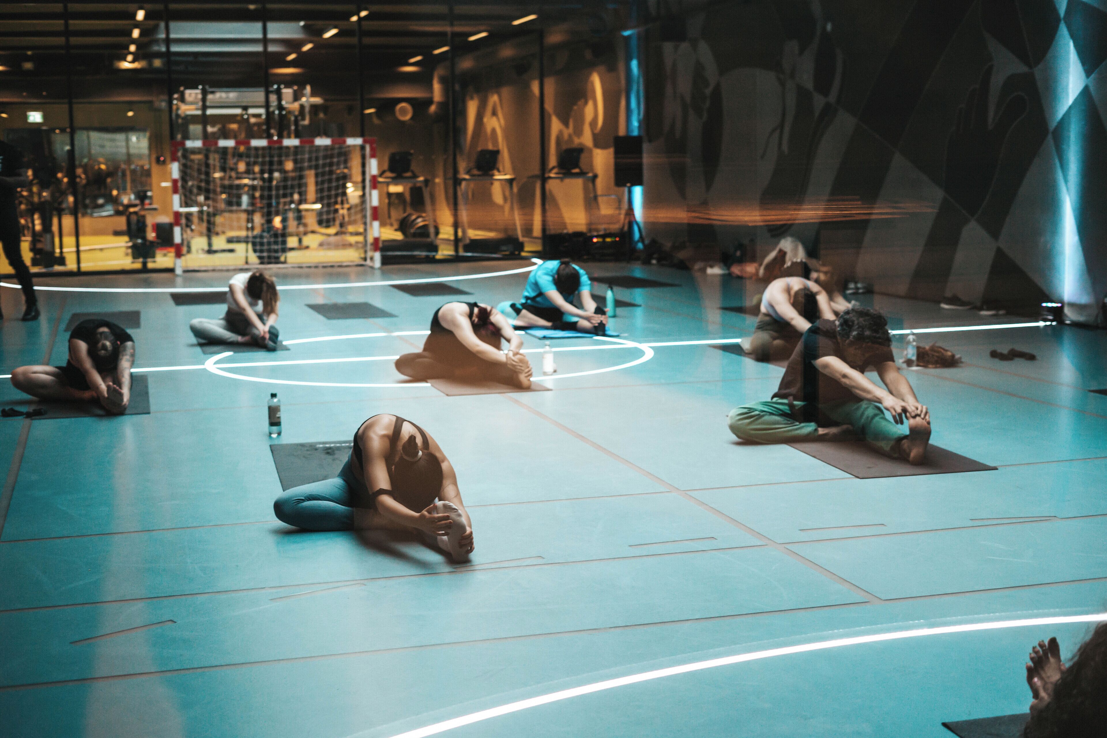 Un grupo de personas practicando yoga en una habitación amplia y moderna, con un espejo grande y equipo de ejercicio al fondo.