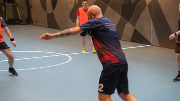En basketballbane med spillere i bevægelse, en basketball og en væg med geometriske mønstre.