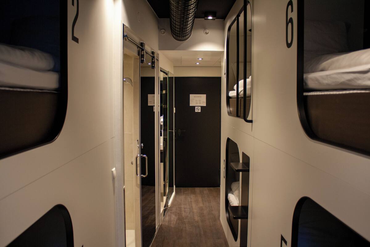 A narrow corridor with bunk beds, each marked with a number. There are glass doors leading to a bathroom, and a sign on the door.