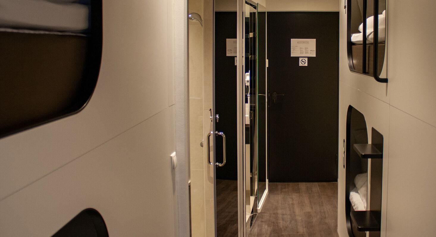 A narrow hallway with a door at the end, a mirror, and a small shelf with a towel.