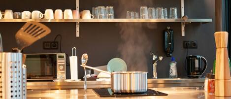 Una cocina con electrodomésticos de acero inoxidable, microondas, cafetera y diversos utensilios en la encimera.